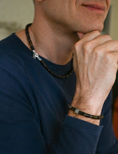 Load image into Gallery viewer, Man wearing a dark blue shirt with a necklace and bracelet, with a blurred background.