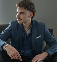 Load image into Gallery viewer, Man in a blue suit with amber necklace and bracelet is sitting on a couch in a neutral setting